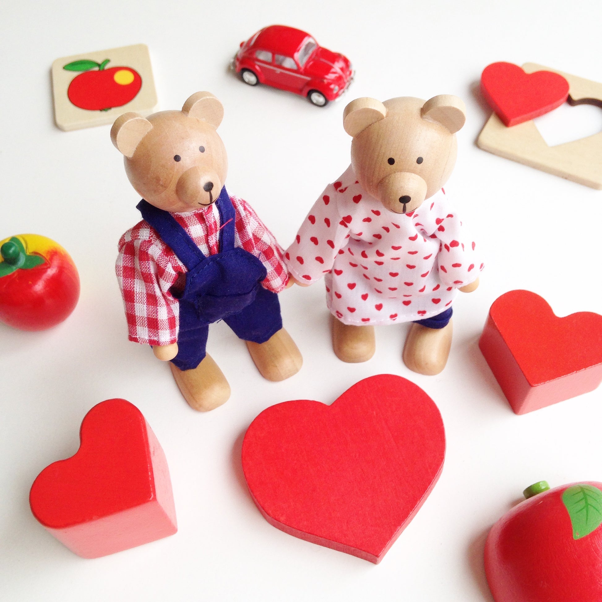 Two teddy bears holding hands with red hearts and toy cars on a white background